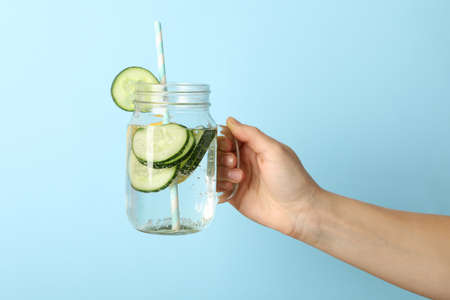 Woman hand hold glass jar with cucumber water, space for text