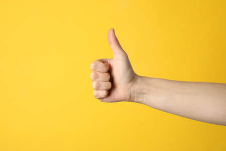 Female thumbs up on yellow background, space for textの写真素材
