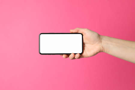 Female hand holds phone on pink background. Empty screenの写真素材