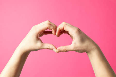 Woman holds hands in the shape of a heart on pink background