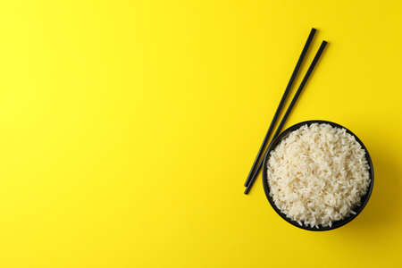 Bowl with boiled rice and chopsticks on yellow background, space for textの写真素材