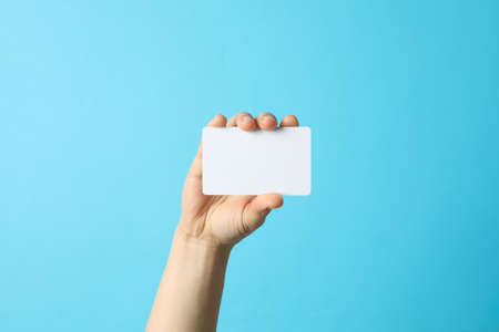 Female hand holding empty business card on blue background