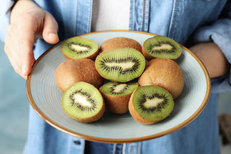 Woman in shirt holding plate of ripe kiwi, close upの写真素材