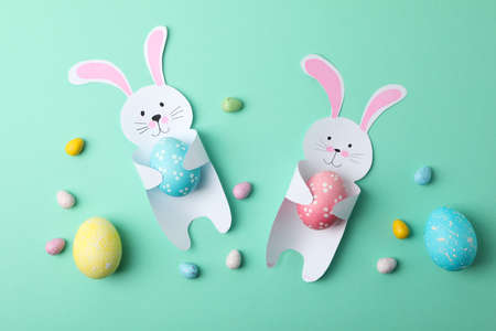 Decorative bunnies and Easter eggs on mint background, top view