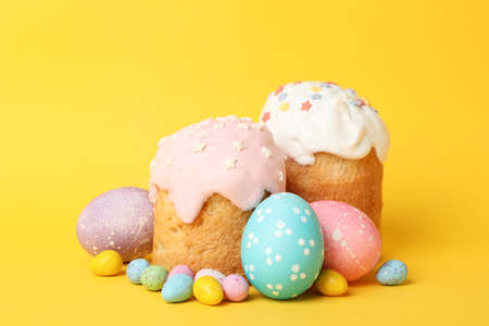 Easter eggs and cakes on yellow background, space for text