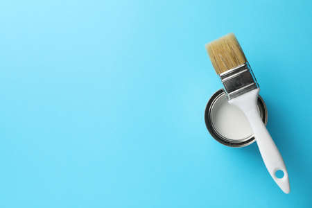 Paint can and brush on blue background, top view