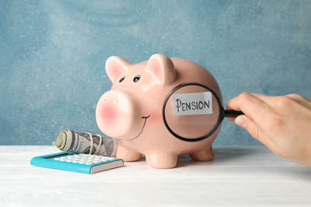 Woman holds magnifier on piggy bank with inscription Pension against blue backgroundの写真素材