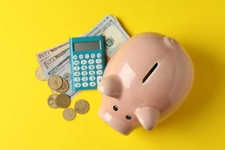 Piggy bank, money and calculator on yellow background, top view