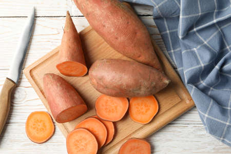Sweet potato, knife, board and towel on wooden background, top view