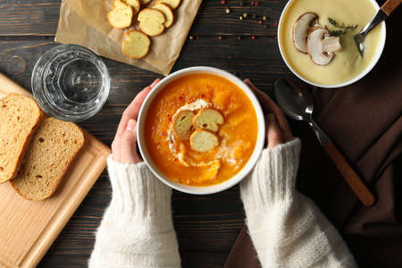 Woman hold bowl with pumpkin cream soup on wooden background, top viewの写真素材