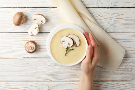 Female hand and mushroom cream soup on wooden background, top viewの写真素材