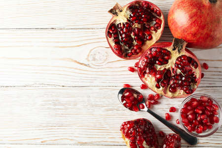 Pomegranate, bowl and spoon on wooden background, top view
