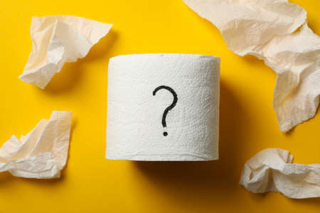 Toilet paper with question mark on yellow background, close up