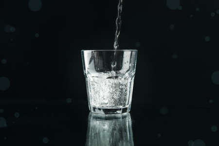 Pouring purified fresh water in glass on mirror background