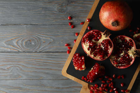 Board with pomegranate on wooden background, top view