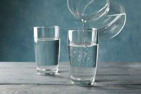 Pouring purified fresh water from the jug in glass on wooden table