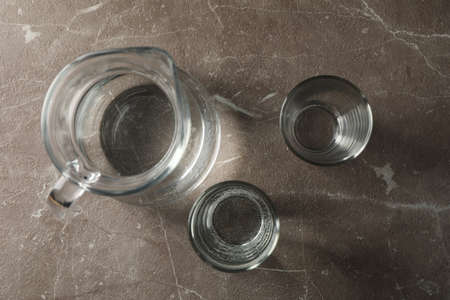 Jug with water and glasses on gray table, top view
