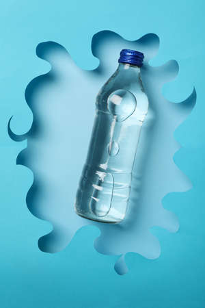 Bottle with water on decorative blue background, top view