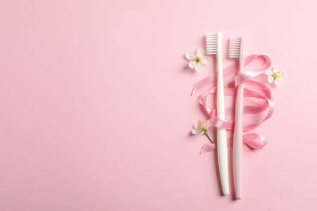 Toothbrushes, ribbon and flowers on pink background, space for textの写真素材