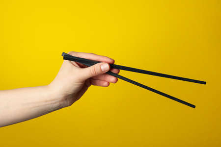Female hand with chopsticks on yellow background, close upの写真素材