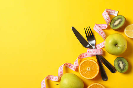 Cutlery, measuring tape and fruits on yellow backgroundの写真素材