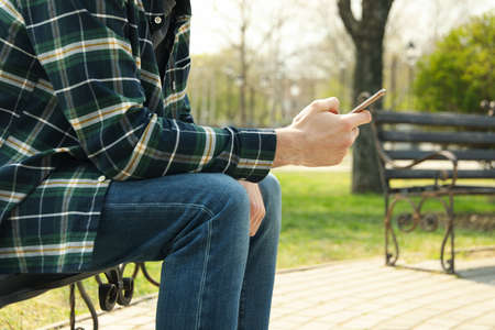 Man uses smartphone sitting on bench in parkの写真素材