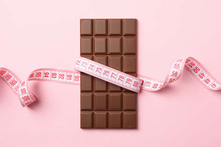 Measuring tape and chocolate bar on pink background