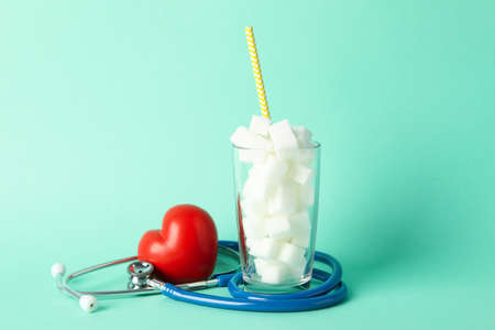 Glass with sugar cubes, heart and stethoscope on mint backgroundの写真素材