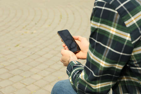Man in shirt uses smartphone sitting in parkの写真素材