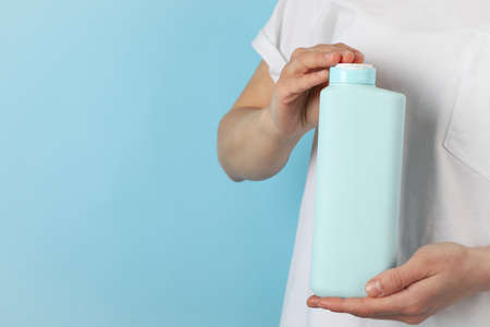Woman holds blank shampoo bottle on blue background, space for text