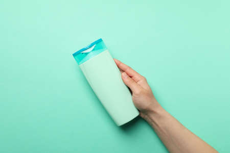 Female hand holds shampoo bottle on mint background, space for textの写真素材