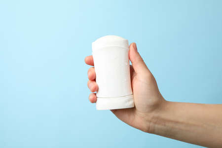 Female hand holds body deodorant on blue background, blank space for textの写真素材