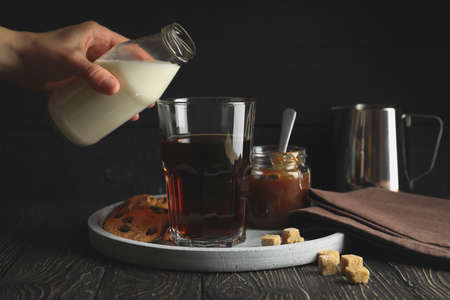Woman pours a milk in glass of coffee. Composition with ice coffee