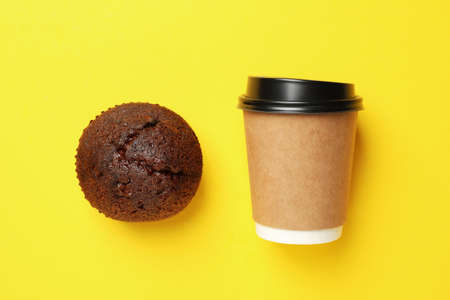 Paper cup and chocolate muffin on yellow background, space for textの写真素材