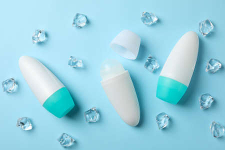 Body deodorant rolls and ice cubes on blue background, top view
