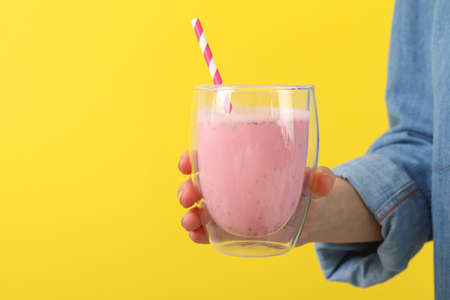 Woman holds glass of strawberry milkshake against yellow backgroundの写真素材