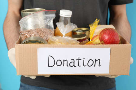 Young man holds donation box against blue background. Volunteerの写真素材