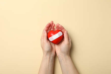 Female hands hold heart with adhesive plaster on beige background, top viewの写真素材