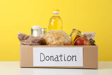 Donation box with different food against yellow background. Volunteeringの写真素材