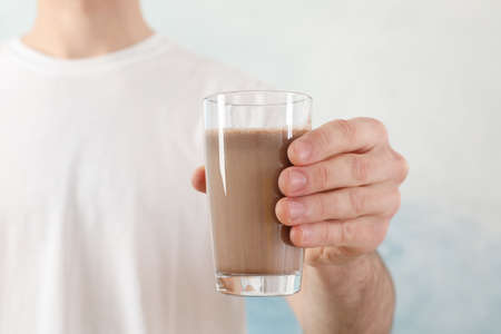 Young man holds glass of chocolate milkshake against blue backgroundの写真素材