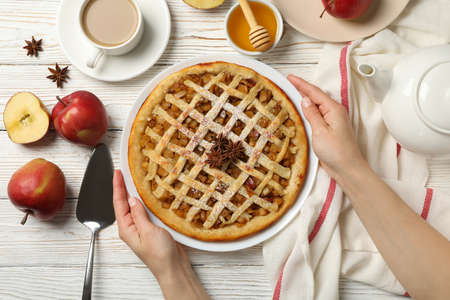 Female hands hold plate with apple pie on white wooden background, top viewの写真素材