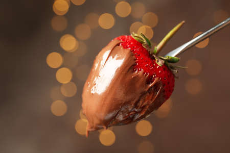 Chocolate fondue. Strawberry in chocolate against brown background with blurred lights