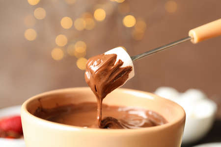 Marshmallow in chocolate against brown background with blurred lightsの写真素材