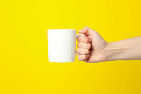 Female hand holding white cup on yellow background, space for text