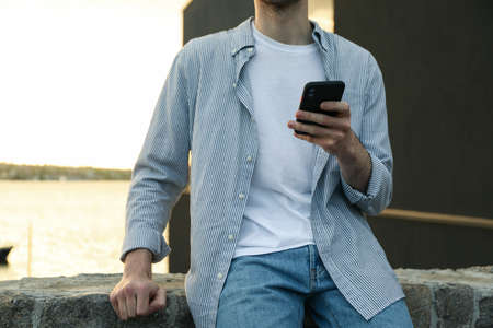 Young man uses a phone outdoor. Writing a messageの写真素材