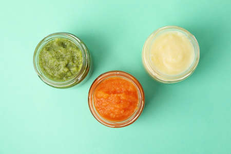 Glass jars with vegetable puree on mint background. Baby food
