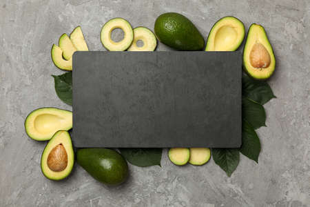 Avocado, leaves and board with space for text on gray background