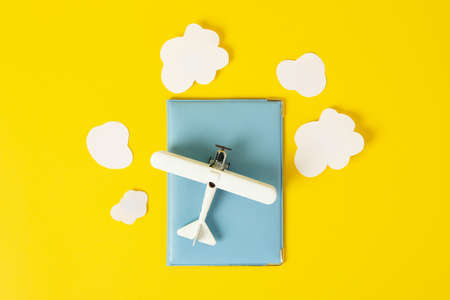 Passport, toy plane and decorative clouds on yellow background, top viewの写真素材