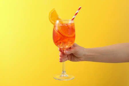 Female hand with glass of aperol cocktail on yellow backgroundの写真素材