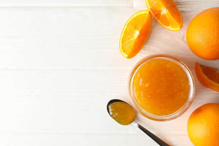 Oranges, spoon and glass jar with jam on white wooden background
